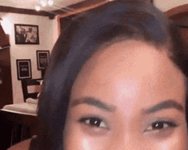 a close up of a woman 's face in a room with pictures on the wall