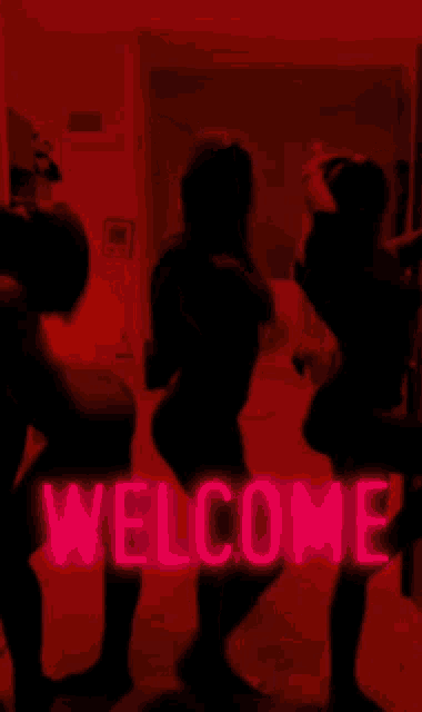 two women are dancing in front of a red welcome sign