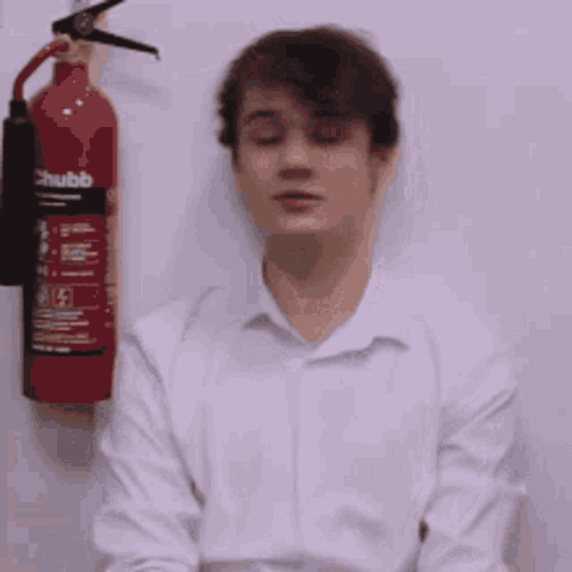 a man in a white shirt is sitting in front of a fire extinguisher hanging on a wall .