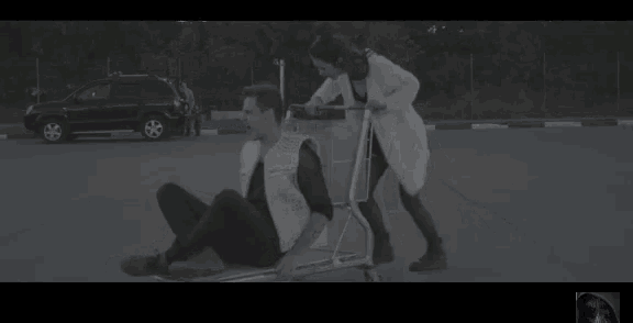 a woman is pushing a shopping cart with a man in it