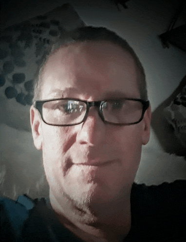 a man wearing glasses and a black shirt looks at the camera