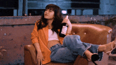 a woman is sitting on a couch holding a bottle of wine with a label that says " pure " on it