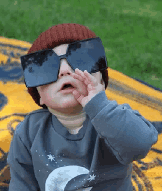 a baby wearing sunglasses and a beanie is covering his eyes