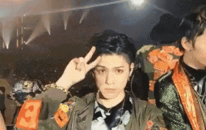 a man is making a peace sign with his finger on his forehead while standing next to another man .