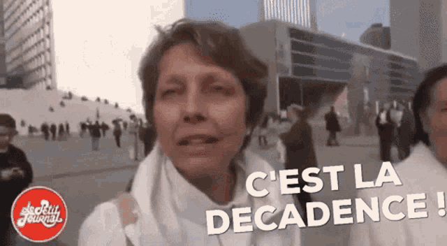 a woman in a white shirt says " c'est la decadence " in front of a crowd of people