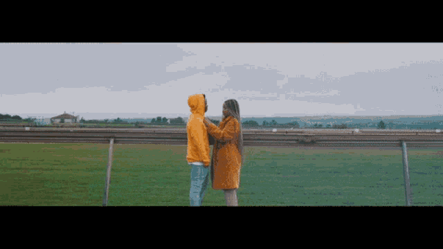 a man and a woman in yellow jackets are standing in a grassy field