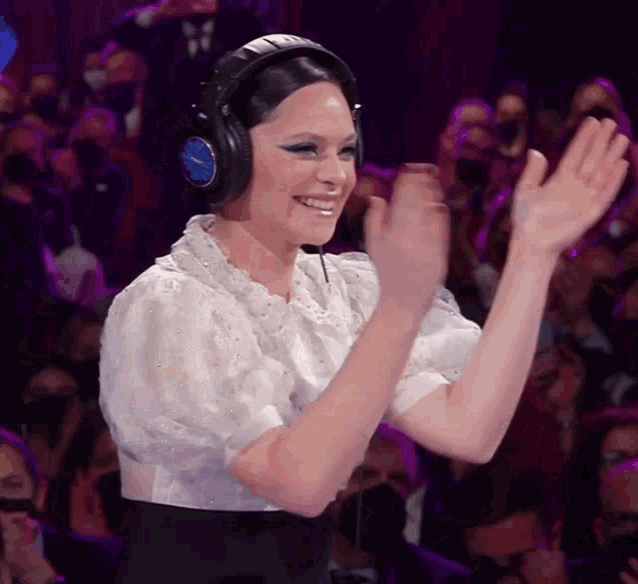 a woman wearing headphones applauds in front of a crowd of people
