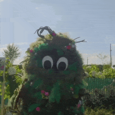 a monster made of leaves and flowers has googly eyes on its face