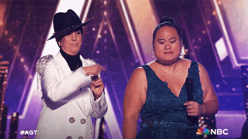 a woman in a blue dress stands next to a man in a white suit on a stage with the nbc logo on the bottom