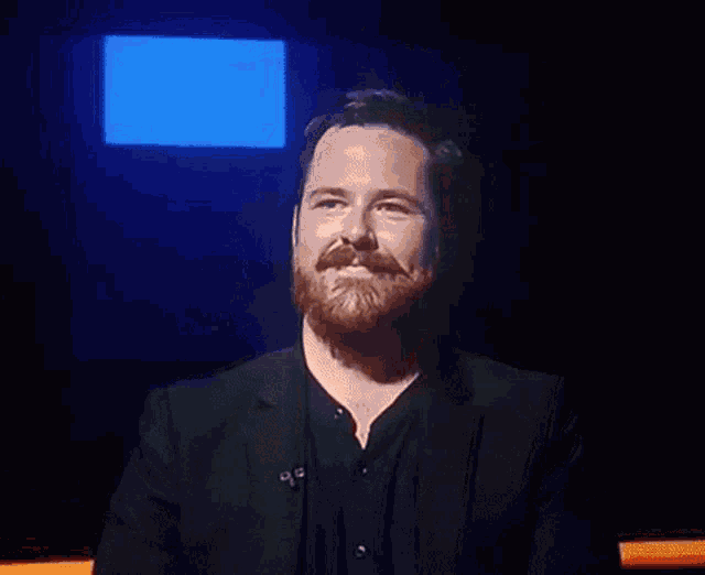 a man with a beard wearing a black suit is smiling
