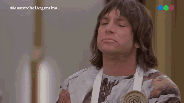 a man with long hair is wearing an apron and making a funny face .