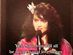 a woman with a flower in her hair is speaking into a microphone and says yes soon you will all be my personal love slaves