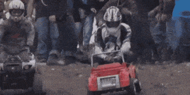 a person wearing a helmet is driving a toy car on a dirt road