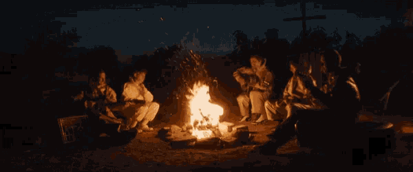 a group of people are sitting around a fire with a sign that says enter here