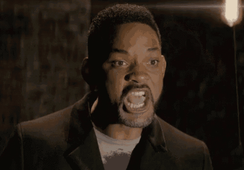 a man with a beard is making a funny face with his mouth open in a dark room .