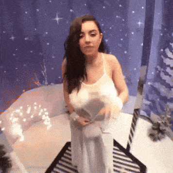 a woman in a white dress is standing in front of a purple curtain and a couch .