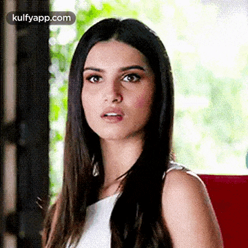 a woman with long hair is wearing a white tank top and making a funny face .