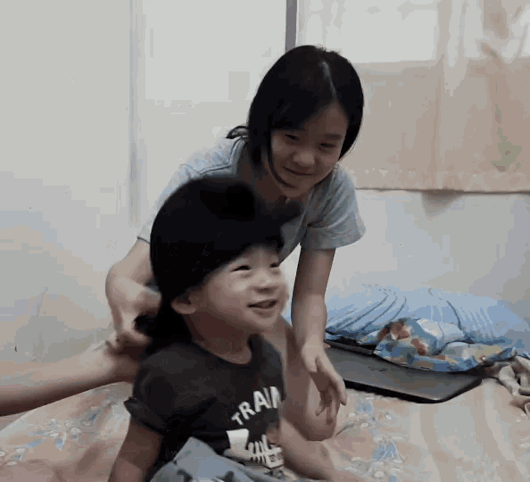 a little girl is putting a hat on a little boy who is wearing a shirt that says train