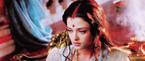 a woman with red hair and a red dot on her forehead is sitting on a throne .