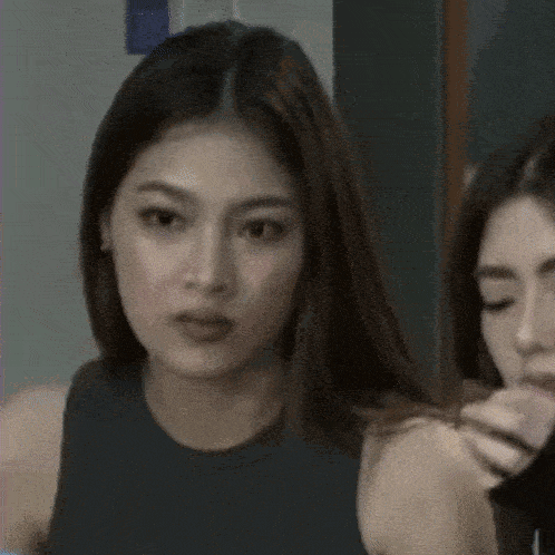 two women are sitting next to each other in a room . one of the women is looking at the camera .