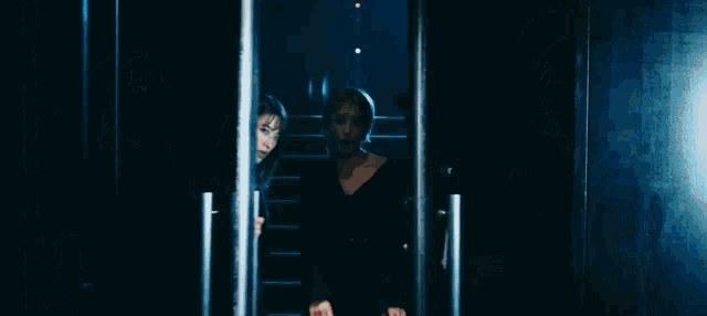 three women are standing next to each other in a dark room with stairs in the background