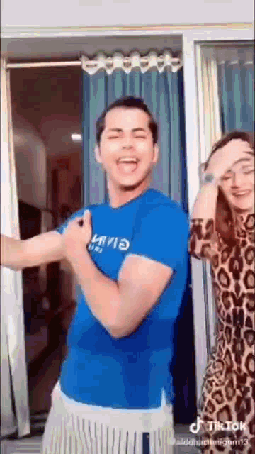 a man in a blue shirt and a woman in a leopard print dress are dancing in front of a sliding glass door .