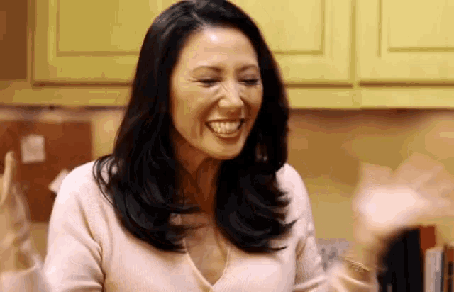 a woman in a pink sweater is smiling in a kitchen with yellow cabinets .