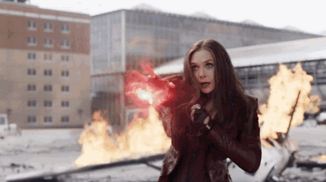 a woman in a red jacket is standing in front of a building that is burning