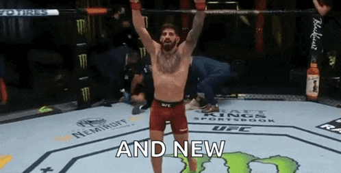a man is standing in a boxing ring with his arms in the air and the words `` and new '' above him .