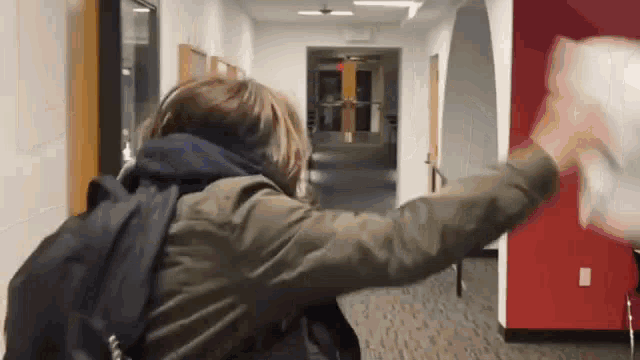 a person with a backpack is walking down a hallway and throwing a piece of paper in the air .