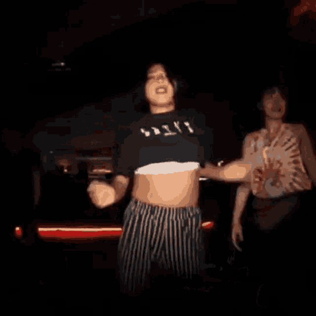 a man and a woman are dancing together in a dark room . the man is wearing a crop top .