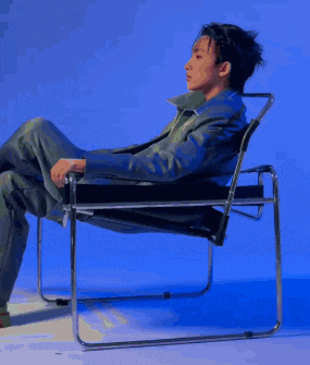a man in a suit is sitting in a chair with his legs crossed and his face painted .