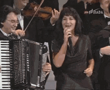 a woman singing into a microphone while playing an overrini accordion