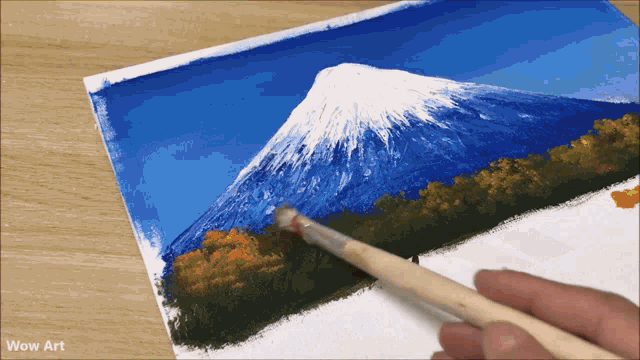 a painting of a mountain is being painted on a piece of paper with wow art written on the bottom
