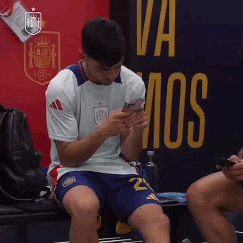 a man in a white shirt with the number 21 on his shorts is looking at his phone