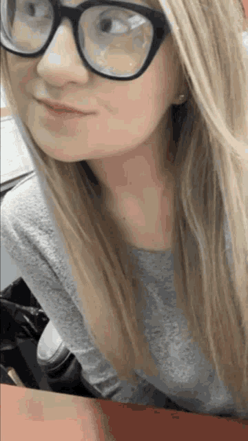 a woman wearing glasses and a grey shirt is smiling