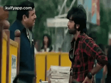 two men are standing next to each other on a sidewalk and talking to each other .