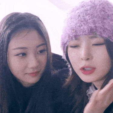a woman wearing a purple hat looks at another woman 's face