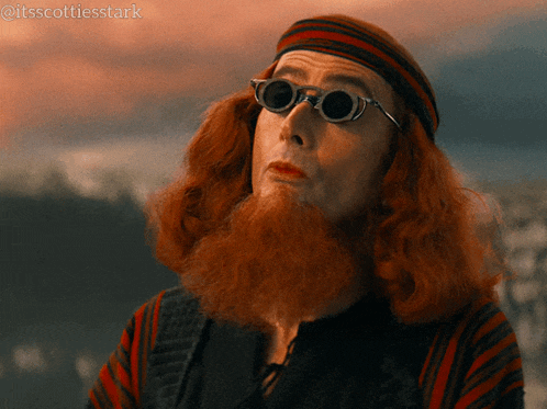 a man with red hair and a beard wears sunglasses and a headband