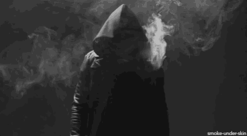 a person in a hooded jacket is smoking a cigarette in a dark room