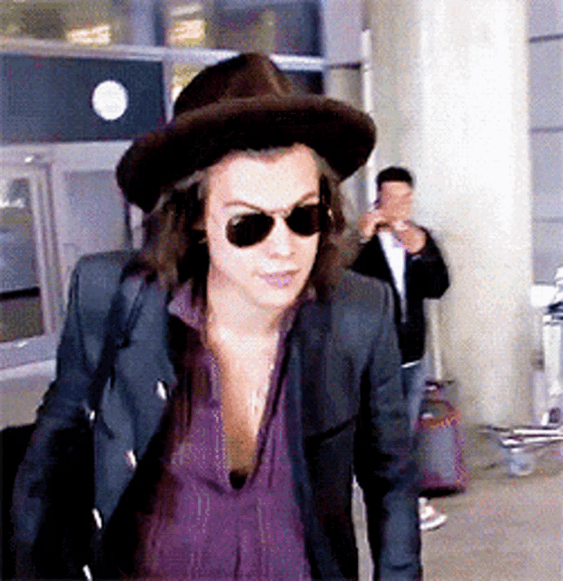a man wearing a hat and sunglasses is walking through an airport