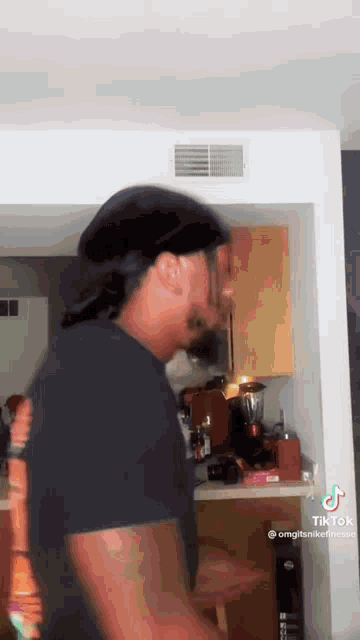 a man in a black shirt is standing in a kitchen with a blender in the background .
