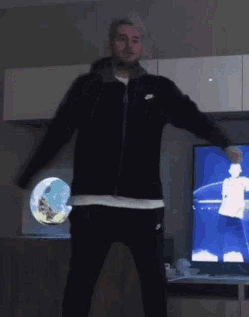 a man in a nike jacket is standing in front of a tv