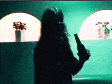 a woman is holding a bottle of beer in front of a green wall