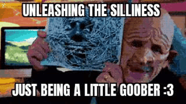 a bald man is holding a piece of paper with a picture of a face on it and making a funny face .