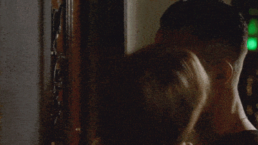 a woman kissing a man 's neck in front of a green light