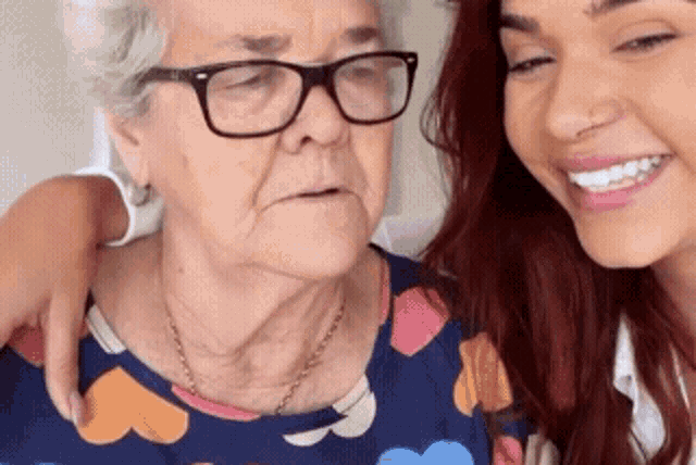 an elderly woman wearing glasses is being hugged by a younger woman with red hair