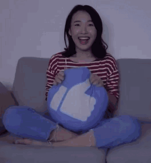 a woman is sitting on a couch holding a blue pillow with a thumbs up symbol on it