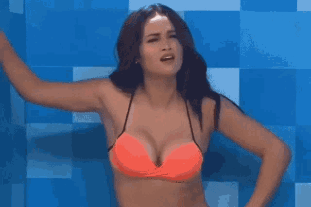 a woman in an orange bikini stands in front of a blue wall