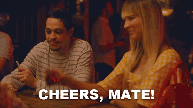 a man and a woman sitting at a table with the words cheers mate